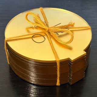 A close up photo of a stack of twenty gold mirror acrylic table numbers, tied in a bundle with gold string. The string is tied off with a knot on top, in the shape of a bow, like a gift or present. They are ready for packing and shipping.